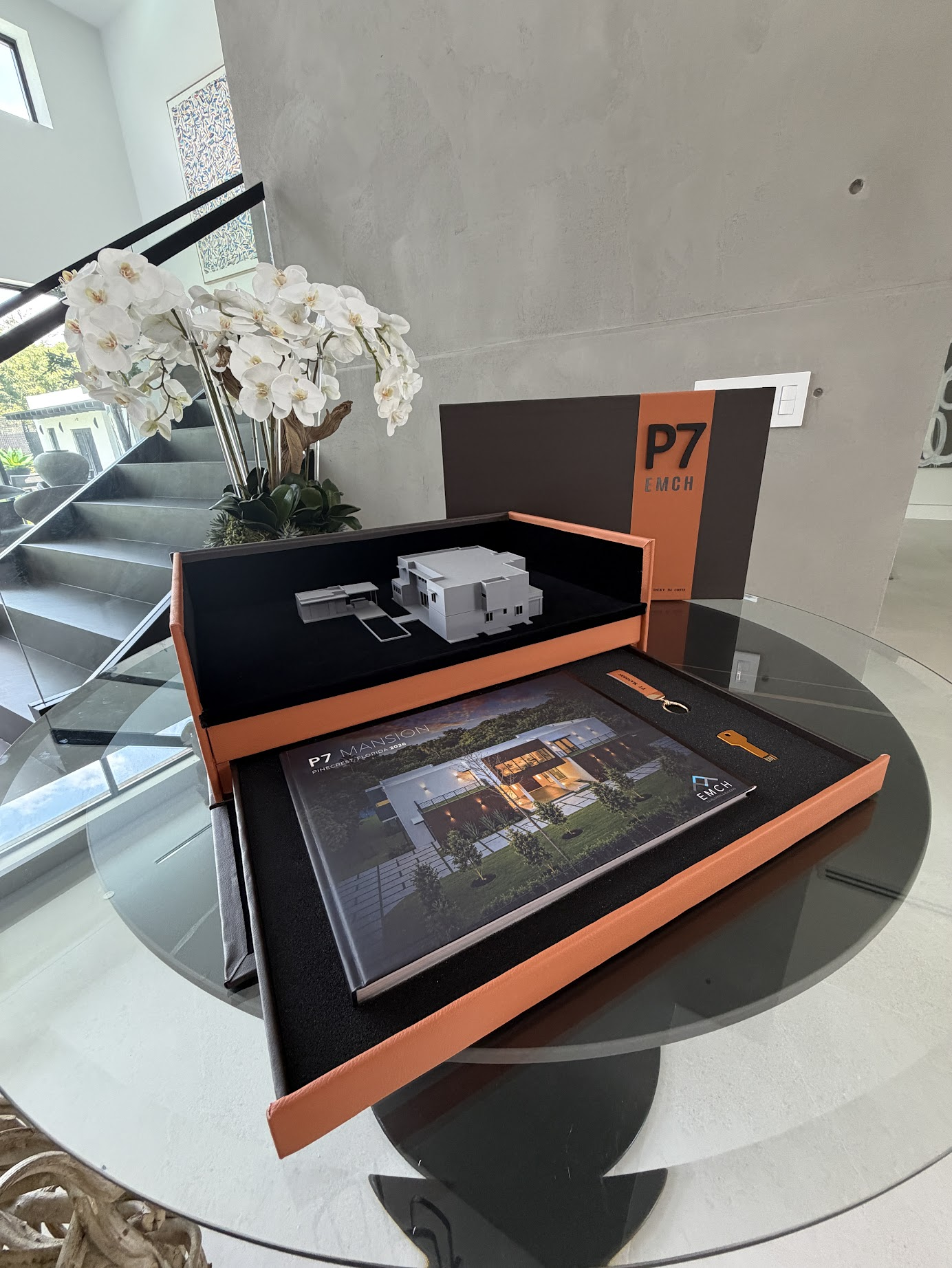La caja de presentación de Casa Completa abierta — la maqueta 3D de la casa, el libro del proyecto y su llave de presentación